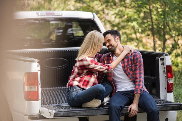 Beautiful couple sitting on pickup truck and looking at each other in forest — Stock Photo