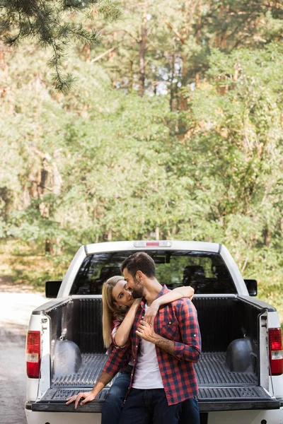 Petite amie étreignant son petit ami tout en étant assis sur le pick-up dans la forêt — Photo de stock