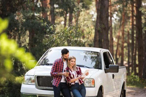 Glückliches Paar nutzt digitales Tablet in der Nähe von Pickup-Truck im Wald — Stockfoto