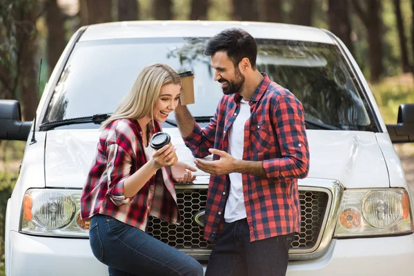 Couple riant avec tasses jetables de café parler près de la voiture — Photo de stock