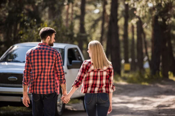 Rückansicht eines Paares, das sich an den Händen hält und im Wald zum Pickup geht — Stockfoto