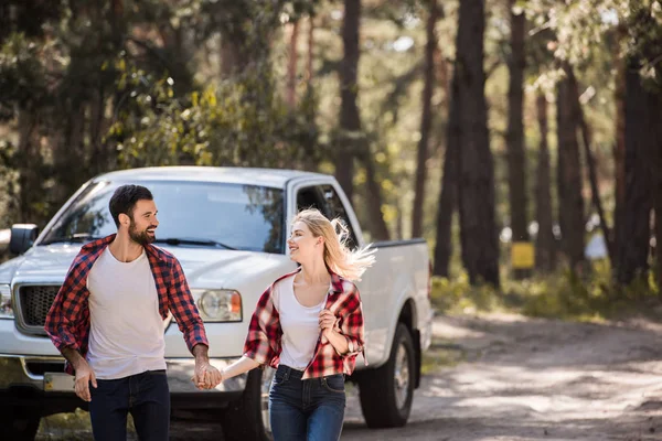 Belo casal alegre de mãos dadas e correndo na floresta com pickup caminhão — Fotografia de Stock