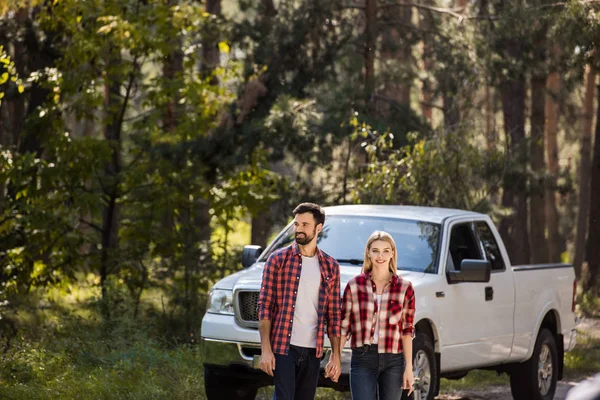 Beautiful couple holding hands and standing near pickup truck in forest — Stock Photo
