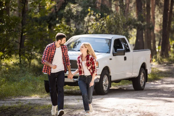 Feliz pareja cogida de la mano y corriendo en el bosque con camioneta - foto de stock
