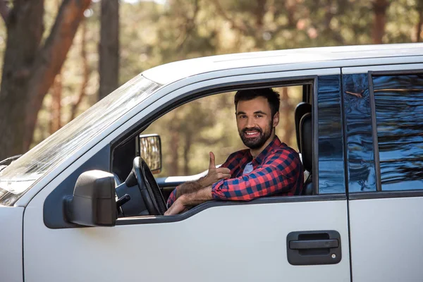 Bearded driver showing thumb up while sitting in pickup truck in forest — Stock Photo
