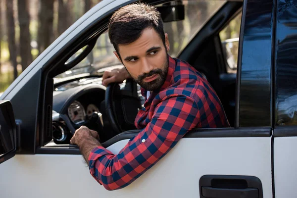 Bearded driver holding steering wheel in pickup truck in forest — Stock Photo