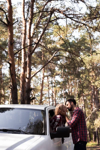 Man kissing girlfriend while she sitting in pickup truck in forest — Stock Photo