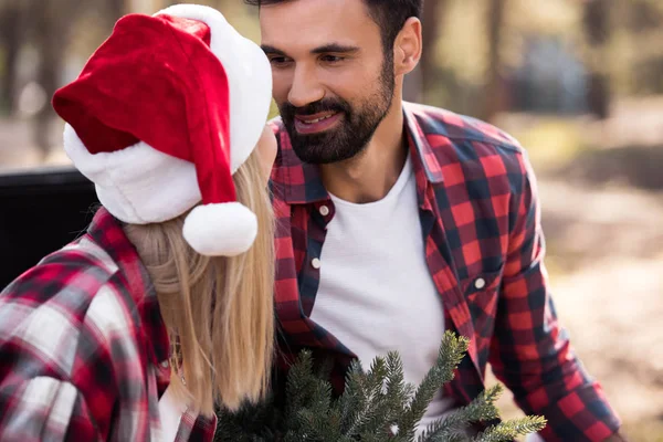 Schönes glückliches Paar in Weihnachtsmannhüten, die einander im Wald anschauen — Stockfoto