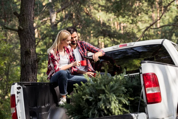 Homme verser du vin dans des tasses tout en étant assis sur la camionnette avec sapin pour Noël dans la forêt — Photo de stock