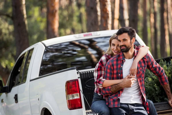 Couple hugging on pickup truck with fir tree for christmas in forest — Stock Photo