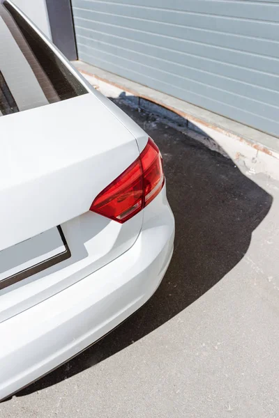 Cropped image of red rear headlight on white car on street near garage — Stock Photo