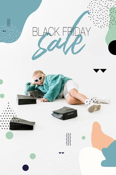 Stylish child in turquoise fur coat lying with black shopping bags on white, black friday sale banner concept — Stock Photo