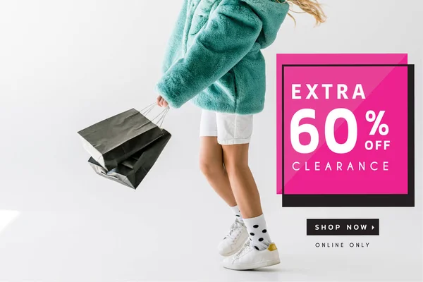 Cropped view of girl in turquoise fur coat holding black shopping bags on white, extra clearance banner — Stock Photo