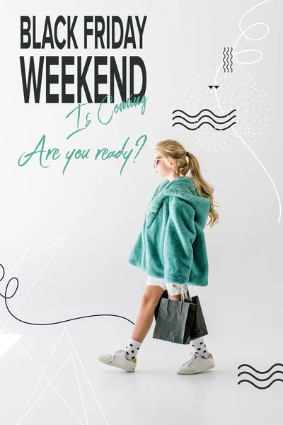 Blonde female child in turquoise fur coat posing with black shopping bags on white, black friday weekend sale banner concept — Stock Photo