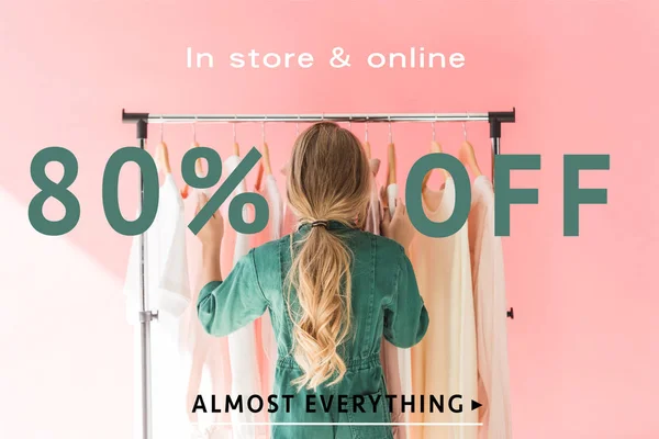 Rear view of blonde kid in trendy overalls choosing clothes on hangers, sale banner concept — Stock Photo