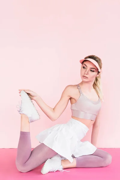 Jeune athlète féminine élégante en chapeau de visière exerçant sur rose — Photo de stock