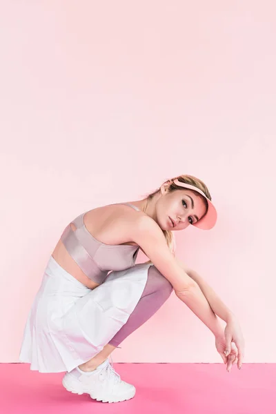 Beautiful stylish female athlete in visor hat posing on pink — Stock Photo