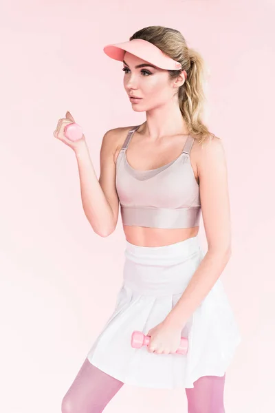 Bonita atleta en sombrero de visera haciendo ejercicio con pesas en rosa - foto de stock