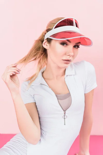 Portrait of beautiful sportswoman in visor hat looking at camera on pink — Stock Photo