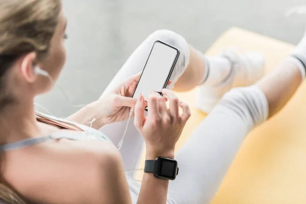 Vue partielle de la sportive avec smartwatch à l'aide d'un smartphone près d'une balle de fitness au gymnase — Photo de stock