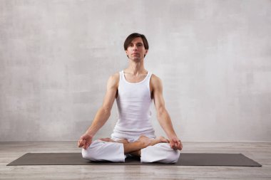 Beyaz elbiseli genç adam oturma odasında yoga yapıyor. Lotus pozu. Meditasyon 