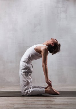 Beyaz elbiseli genç adam yoga yapıyor. Deve pozisyonu. Ustrasana