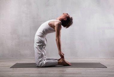 Beyaz elbiseli genç adam yoga yapıyor. Deve pozisyonu. Ustrasana