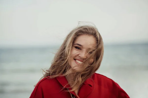Hermosa mujer feliz en abrigo rojo caminando por la playa —  Fotos de Stock