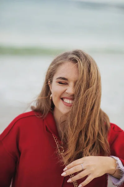 Bella donna ridente in cappotto rosso che cammina sulla spiaggia — Foto Stock