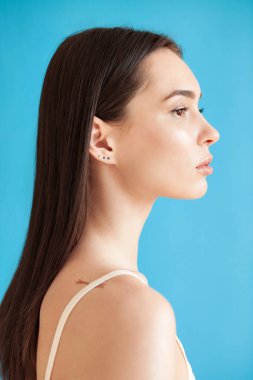 Mavi arka planda, sağlıklı, pürüzsüz bir teni olan güzel bir genç kadının portresi. Günlük güzellik rutini