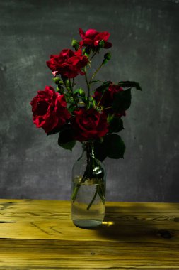 Parlak kırmızı bahçe gül ahşap masa ve koyu arka plan üzerinde.