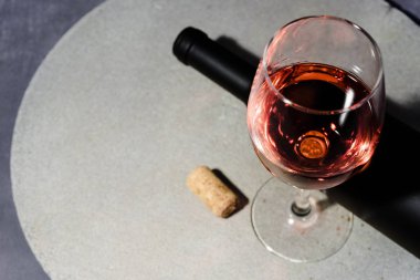 Bardak kırmızı şarap bir yuvarlak taş tabloda siyah bir şişe şarap. Güzel koyu kırmızı arka plan