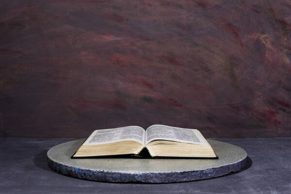 Bible on a round stone table. Beautiful dark-red background. Religious concept.