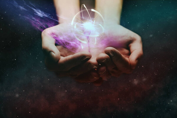 Human hand holding atom on a palm. Nebula dust in infinite space. Mixed media.