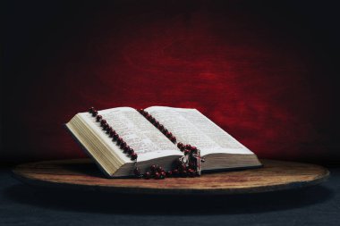 İncil ve eski bir yuvarlak masa üzerinde haç boncuk. Güzel kırmızı ahşap arka plan. Din kavramı.