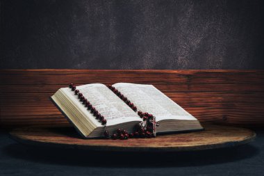 İncil ve eski bir yuvarlak masa üzerinde haç boncuk. Güzel kahverengi ahşap ve gri duvar arka plan. Din kavramı.