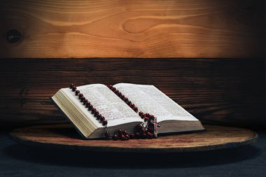 İncil ve eski bir yuvarlak masa üzerinde haç boncuk. Güzel kırmızı ahşap arka plan. Din kavramı.