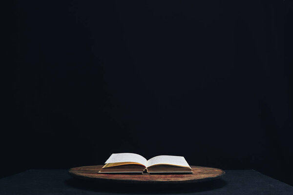 One open old book on a round wooden table. Beautiful dark background