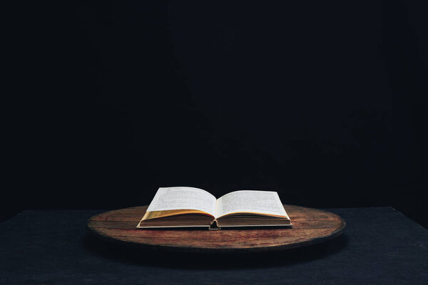 One open old book on a round wooden table. Beautiful dark background