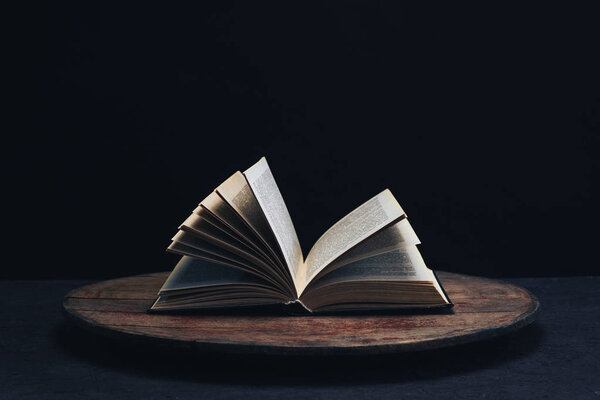 One open old book on a round wooden table. Beautiful dark background