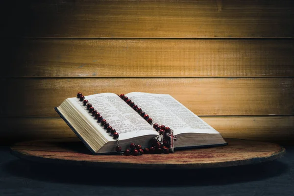 İncil ve eski bir yuvarlak masa üzerinde haç boncuk. Güzel sarı ahşap arka plan. Din kavramı.