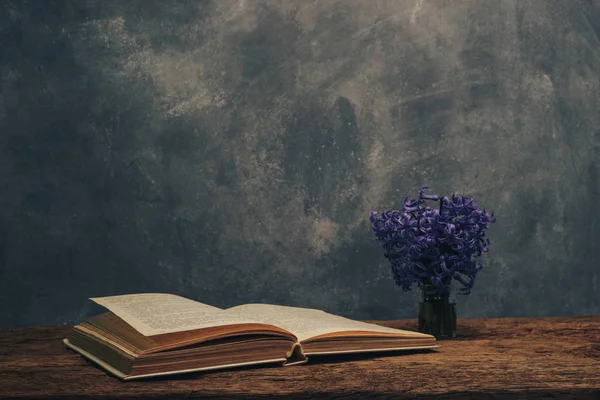 Open book and purple flower on a old  oak wooden table. Gray wall background.