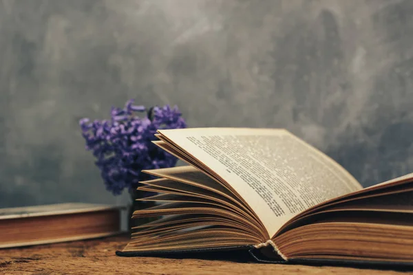 Open book and purple flower on a old  oak wooden table. Gray wall background.