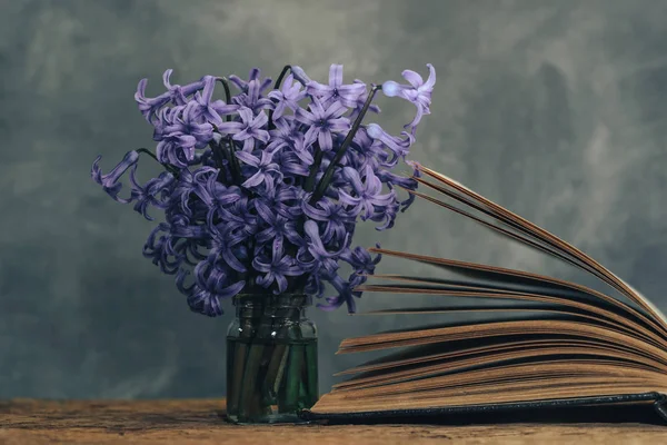 Open book and purple flower on a old  oak wooden table. Gray wall background.