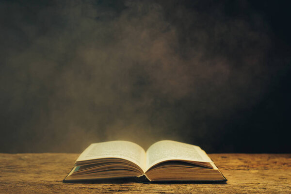 Old book on a oak wooden table. Background of blue and red smoke.