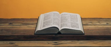 Kutsal İncil 'i eski bir meşe ağacından masanın üzerinde aç. Turuncu duvar arka planı.