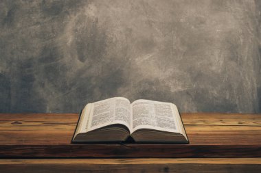 Kutsal İncil 'i eski bir meşe ağacından masanın üzerinde aç. Gri duvar arka planı.