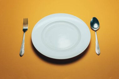 Beyaz kase ve turuncu arka planda kaşıkla çatal.