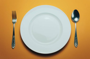 Beyaz kase ve turuncu arka planda kaşıkla çatal.