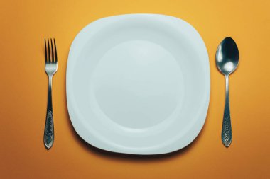 Beyaz kase ve turuncu arka planda kaşıkla çatal.